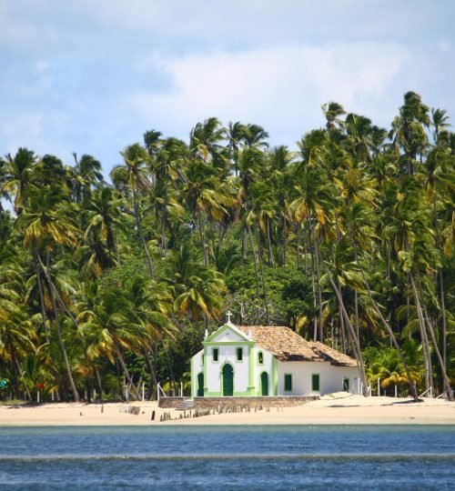 A picturesque church surrounded by palm trees on a sandy beach in Porto de Galinhas, Brazil.