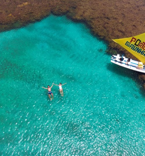 Aerial shot of people swimming near a boat in the turquoise waters of Porto de Galinhas.
